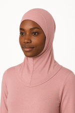 A person wearing a light pink, long-sleeved top with a matching hijab, standing against a neutral background.